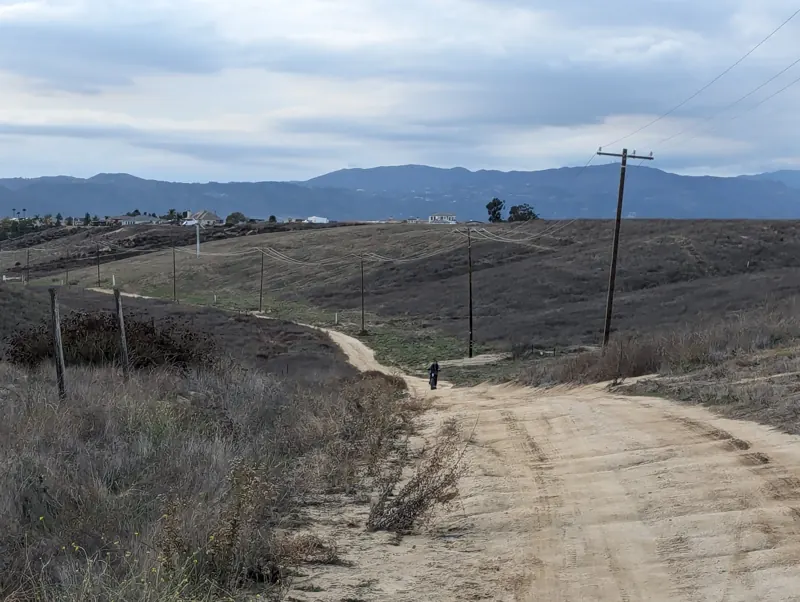 Dirt road winding through the hills with homes and mountains in the distance