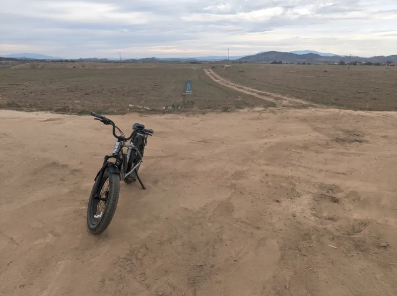 Fat-tire e-bike parked on a dirt road with open fields and mountains beyond